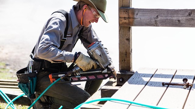 Maintenance worker using a power drill on a boardwalk